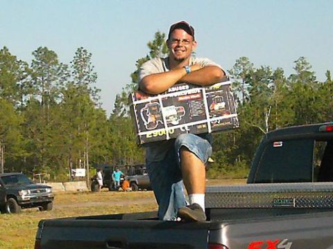 1986 Ford Bronco - Man holds a box of engine parts while standing in the bed of a pickup truck.