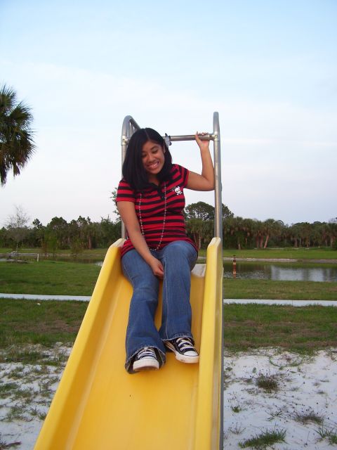 1994 Ford Probe - A young woman enjoys a ride down a yellow slide in a park setting with trees and a pond in the background.