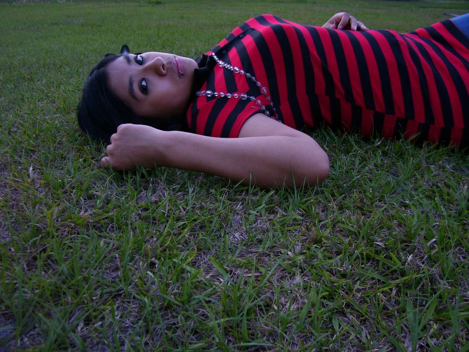 Person in red and black striped shirt lying on grass, looking at camera