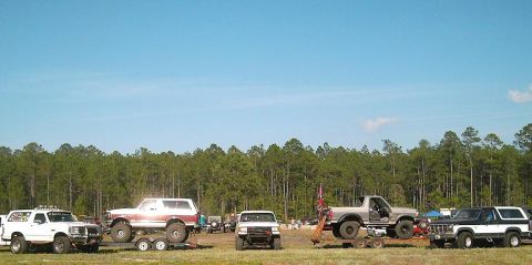 1986 Ford Bronco - Multiple off-road vehicles are gathered in a field under a clear blue sky.