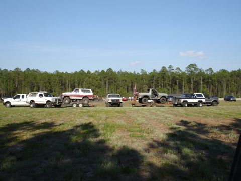 1989 Ford Bronco - Multiple trucks and SUVs are parked in a field, with a 1989 Ford Bronco visible on a trailer.