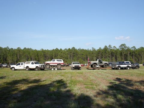 1989 Ford Bronco - A collection of off-road vehicles are gathered in an open field under a clear blue sky.