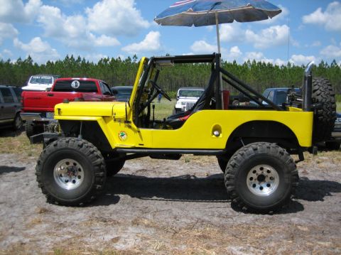 1989 Ford Bronco - A bright yellow Jeep is parked outdoors, a roll cage and a beach umbrella providing shade.