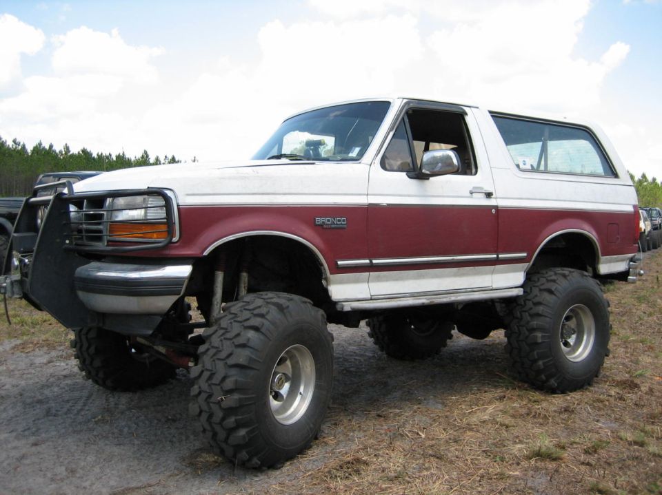 Lifted white and maroon Ford Bronco with big tires and a brush guard