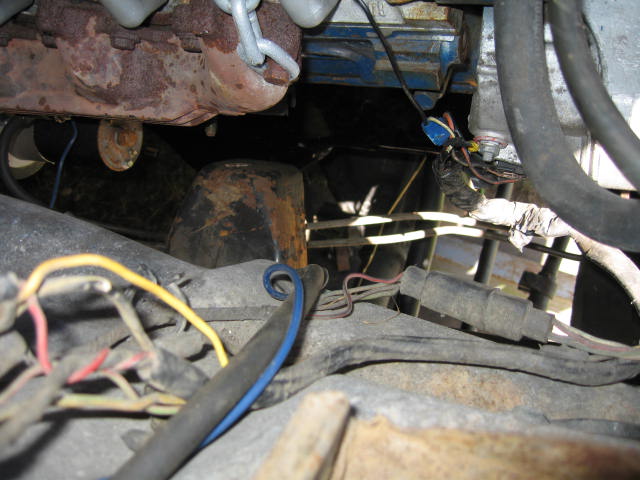 Underhood view of a tangle of frayed wiring, hoses and a rusty exhaust manifold