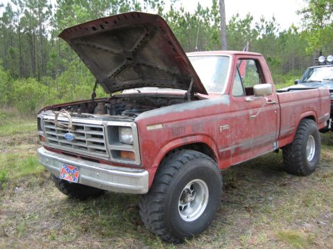 1989 Ford Bronco - This weathered red Ford F-150 pickup truck has its hood raised, revealing the engine bay.