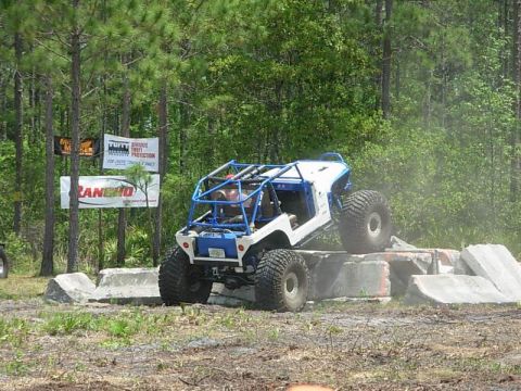 1989 Ford Bronco - Custom off-road buggy navigates concrete obstacles during an event. Supermotors.net logo is present.