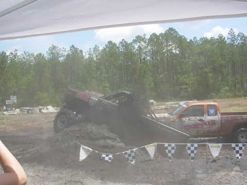 1989 Ford Bronco - Two trucks are engaged in a mud bogging event, with one truck partially submerged in mud.