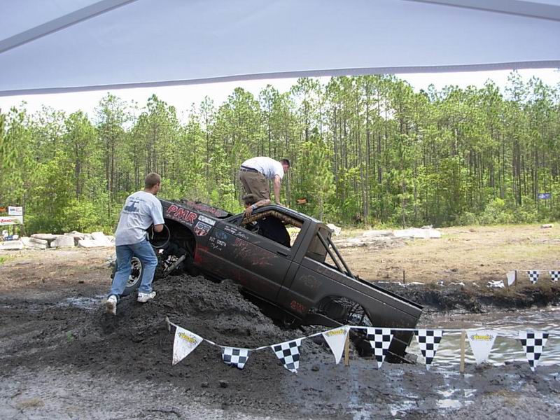 Mud bogging truck stuck in mud with people pushing