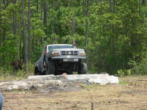 1989 Ford Bronco - This lifted pickup truck is positioned on a concrete obstacle in a wooded area.