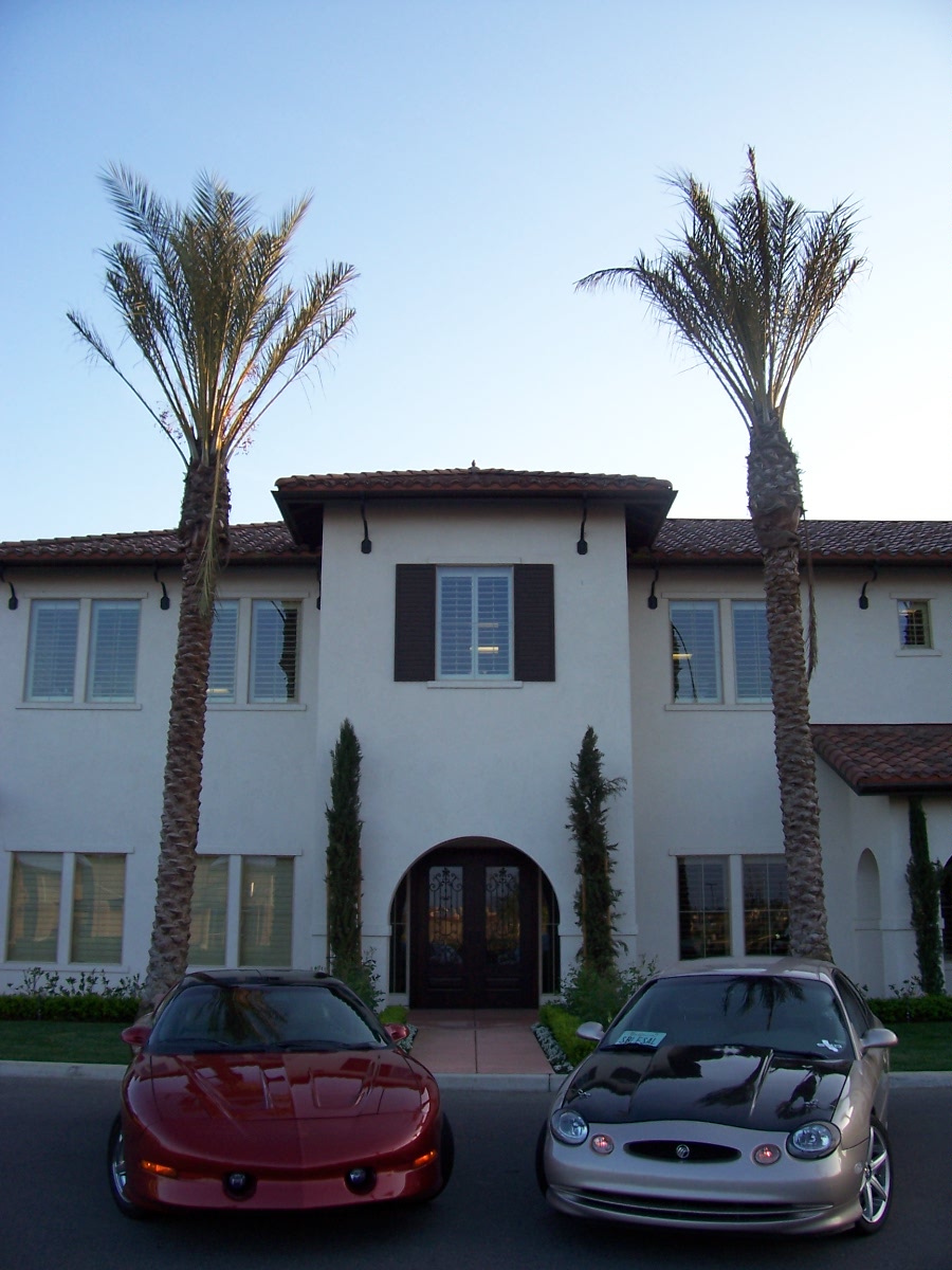 Front view of a red sports car and a tan sedan with a black hood parked in front of a house