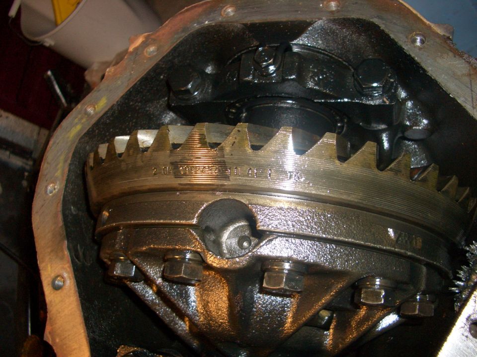 Close-up of an open differential gear assembly with visible teeth and bolts. Text is stamped on the ring gear