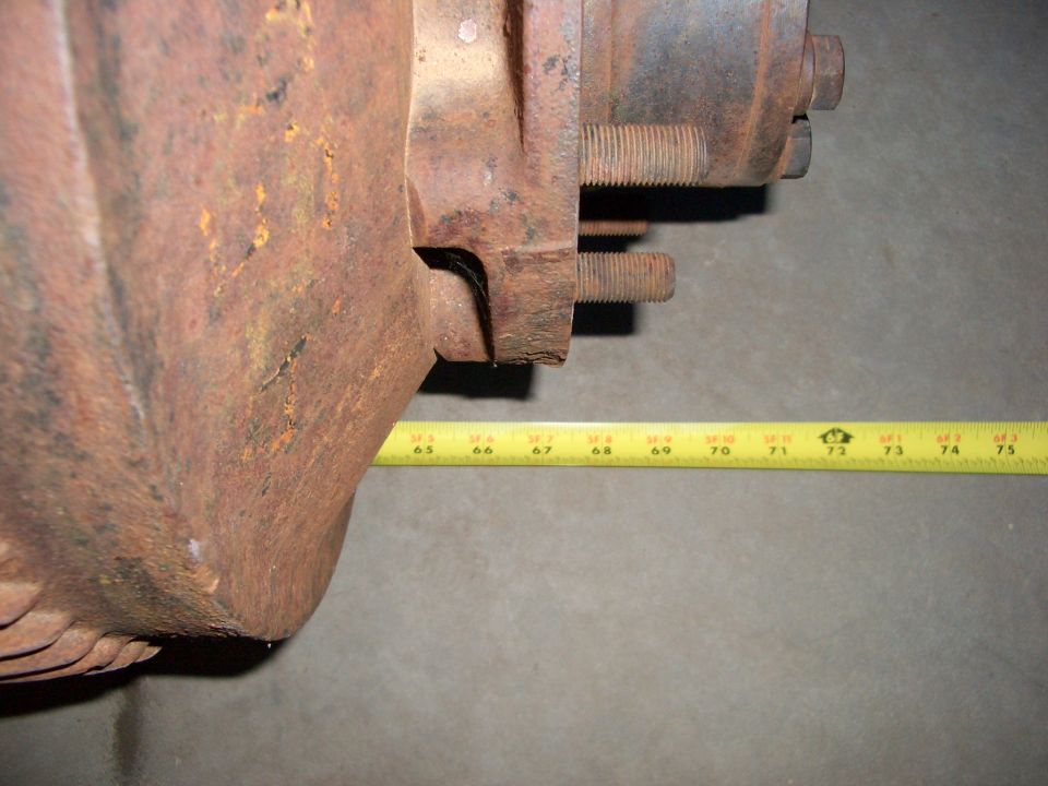 Rusty axle housing with spring perch and studs, yellow tape measure across it