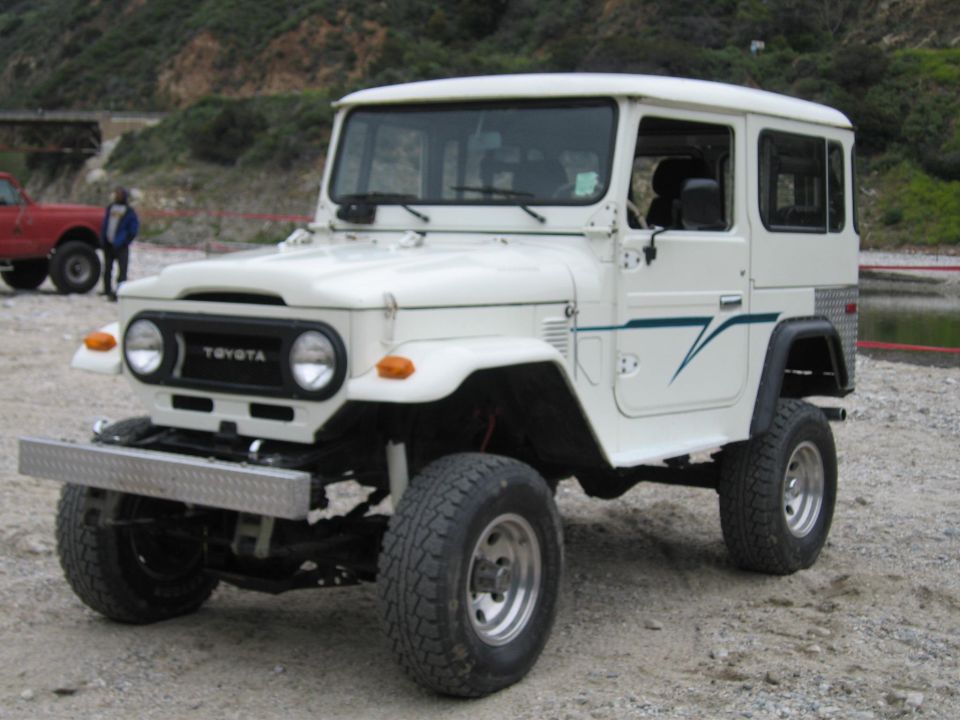 White Toyota FJ40 Land Cruiser hardtop with diamond-plate bumper and teal pinstripe