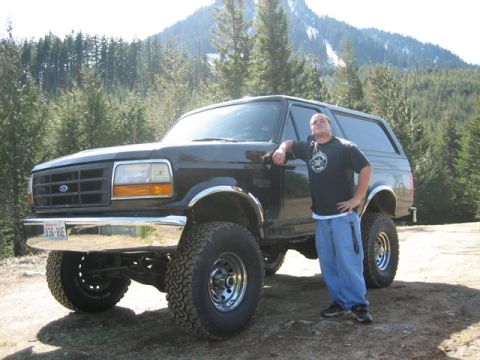 1995 Ford Bronco - A man poses with a lifted black Ford Bronco in a mountainous, wooded area.