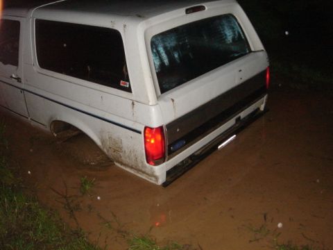1994 Ford Bronco - This white SUV is stuck in muddy water at night. The vehicle appears to be a Ford Bronco.