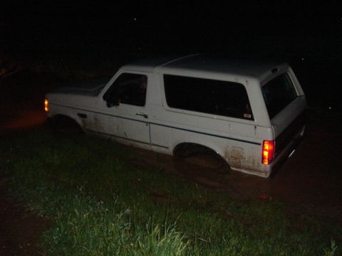 1994 Ford Bronco - A white Ford Bronco is stuck in muddy terrain at night, with its lower half submerged.