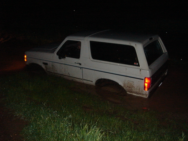 White Ford Bronco stuck in mud at night, side view. Mud covers the lower body and tires