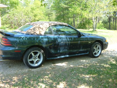 1995 Ford Mustang - A dark green Ford Mustang convertible is parked outdoors on a sunny day.