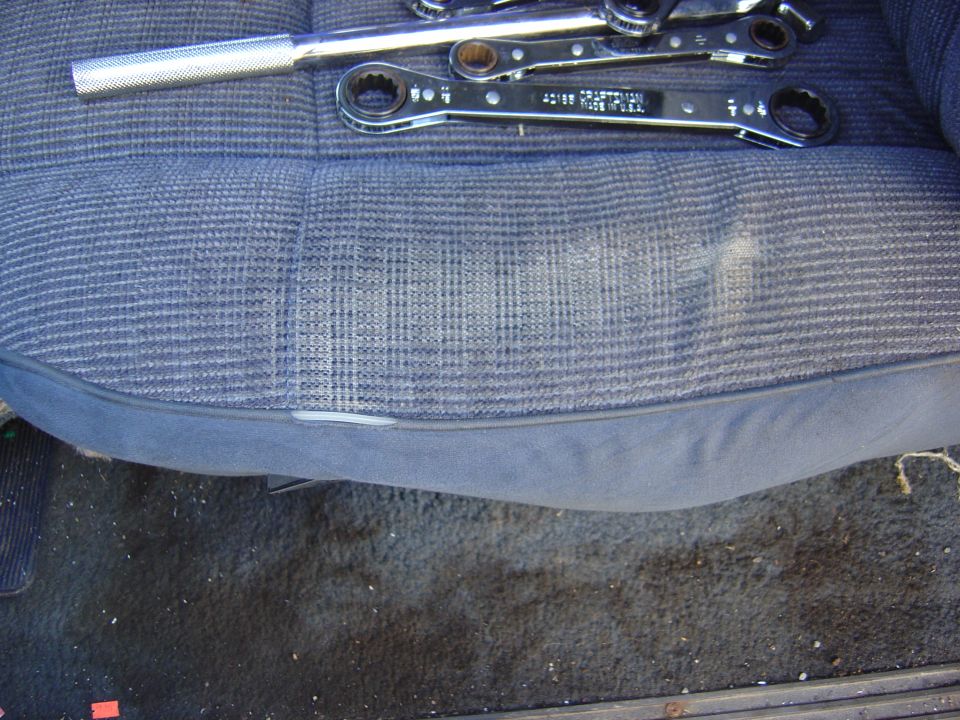 Car seat with plaid fabric and a set of wrenches on top. Floor mat visible