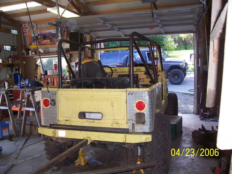 Yellow Jeep CJ body with roll bar on jack stands inside a metal shop, dated 04/23/2006