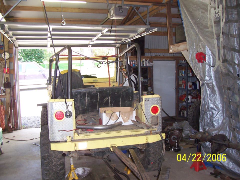 Yellow Jeep tub on jack stands in shop with bare roll cage tacked in and diamond-plate rear corners