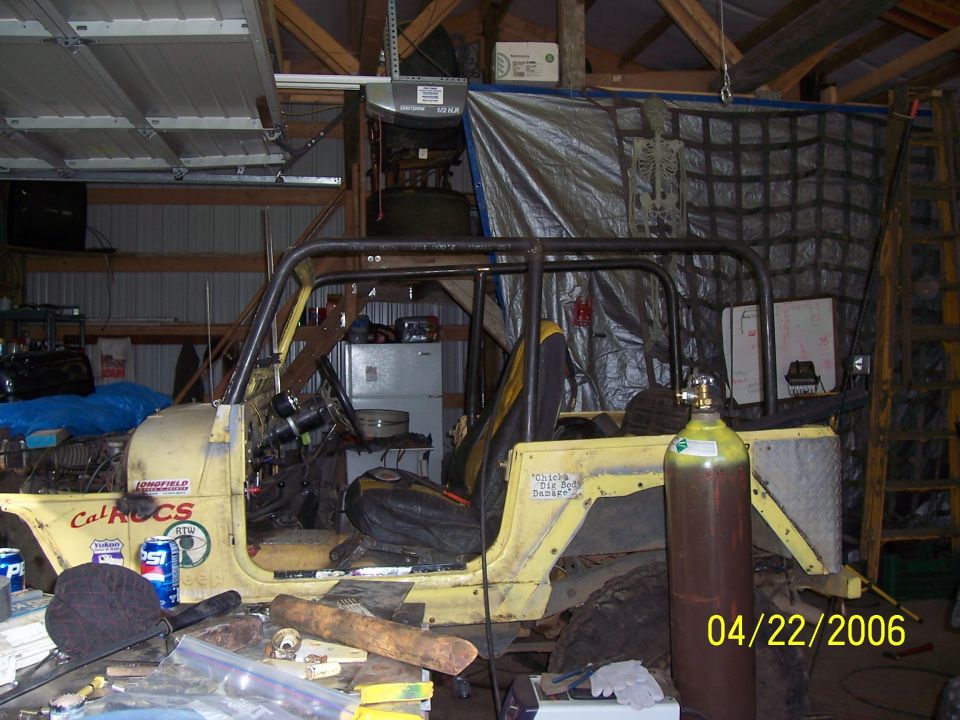 Yellow open Jeep with roll cage and stickers parked in a garage
