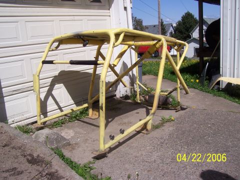 1982 Ford Customline - A yellow roll cage is shown outdoors, resting on the ground in front of a garage door.