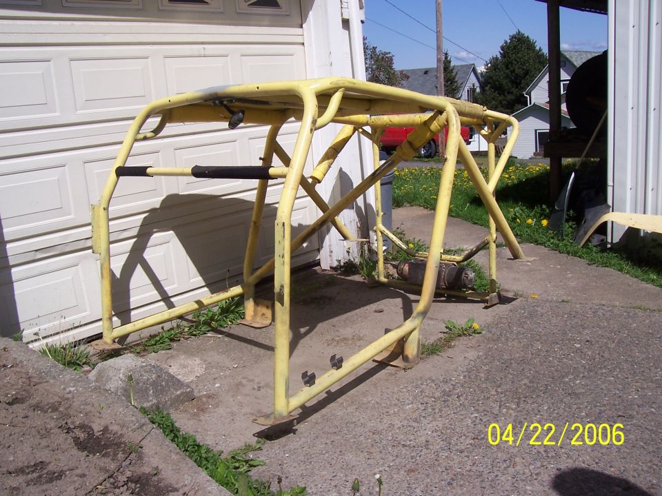 Yellow roll cage removed from vehicle, standing on a driveway by a garage door