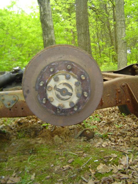 1979 Ford Bronco - A close-up view of a rusty hub and brake rotor assembly is shown in a wooded outdoor setting.