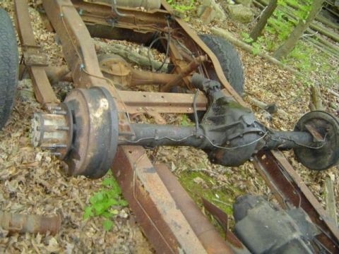 1979 Ford Bronco - The rear axle and frame of a vehicle are visible, resting on the ground amidst debris and foliage.