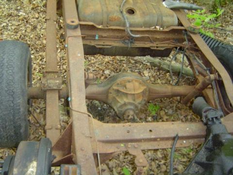 1979 Ford Bronco - The rear axle and fuel tank of a heavily rusted vehicle chassis are shown in this close-up view.