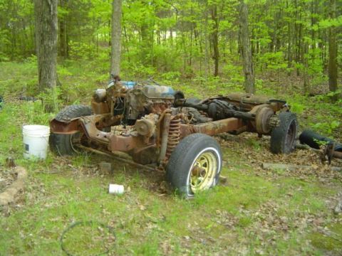 1979 Ford Bronco - This is a rusted vehicle chassis with its engine and wheels, located outdoors in a wooded area.