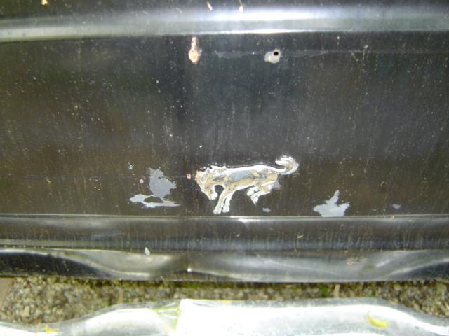 chrome horse emblem on a scratched black panel, possibly a car fender or tailgate