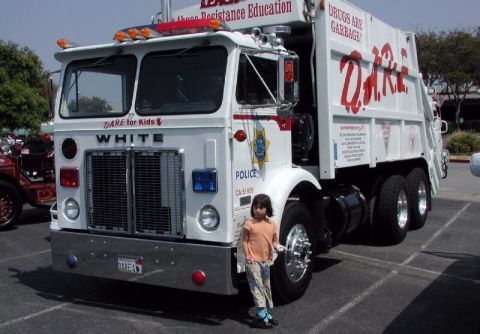1998 Ford Crown Victoria - White garbage truck with DARE logo and "Drugs Are Garbage" text. A child stands next to it.