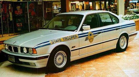 1998 Ford Crown Victoria - A white BMW sedan marked as a state trooper vehicle is shown from the side.