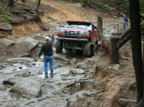 1995 Ford Bronco - A red SUV navigates a challenging off-road trail with steep inclines and large rocks.