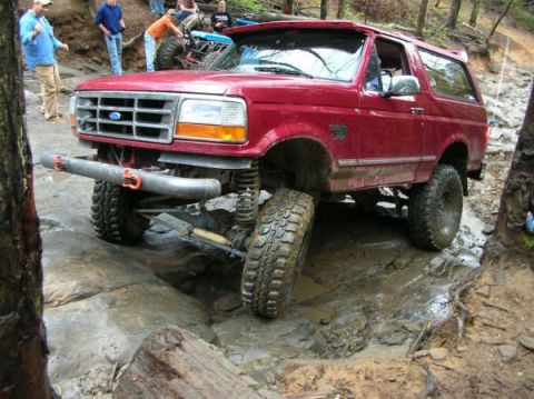 1995 Ford Bronco - This red 1995 Ford Bronco is tackling a challenging off-road course with steep inclines and muddy terrain.