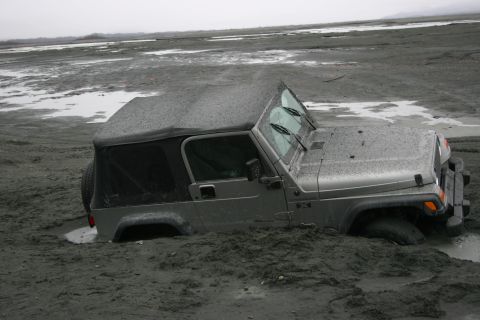 2003 Jeep TJ - A Jeep TJ is deeply stuck in mud, with its front right wheel submerged in the mire.
