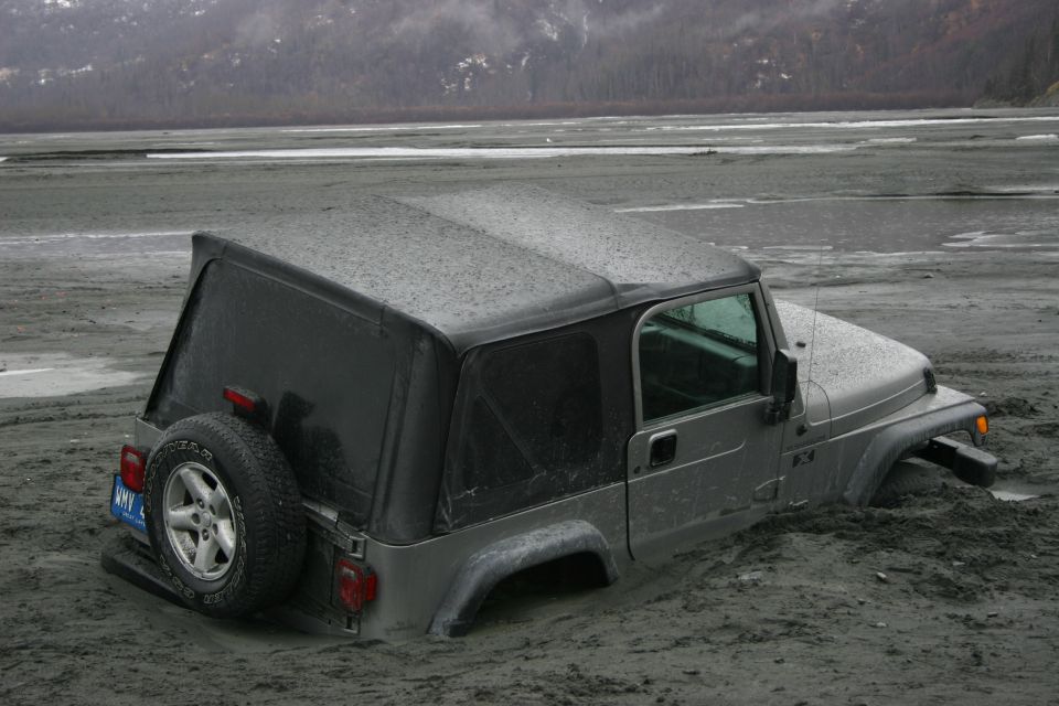Silver Jeep TJ stuck in mud, seen from the front-right three-quarter angle