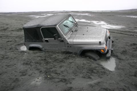 2003 Jeep TJ - A silver 2003 Jeep TJ is deeply stuck in mud, with only the top half of the vehicle visible above the mire.