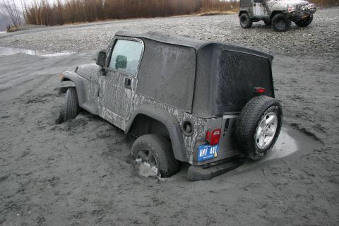 2003 Jeep TJ - A Jeep TJ is stuck in mud, with another Jeep in the background on a gravelly shore.