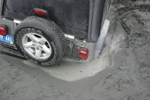 2003 Jeep TJ - A 2003 Jeep TJ is stuck in thick mud, with its rear tire and bumper partially submerged.