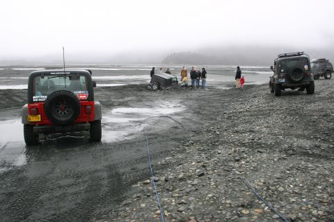 2003 Jeep TJ - A group of people and their Jeeps are on a wet, gravelly terrain, with one vehicle partially submerged in mud.