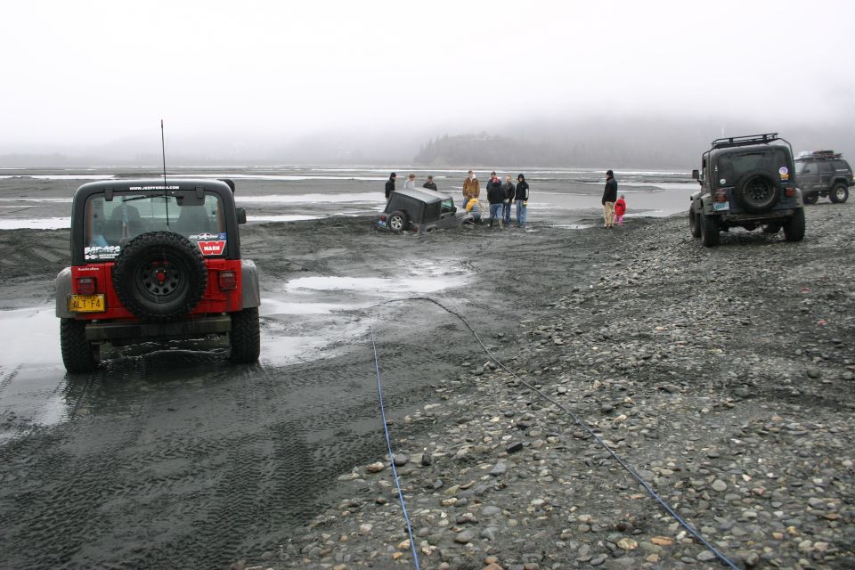 Several Jeeps are on a muddy, rocky plain with people gathered around one that appears stuck
