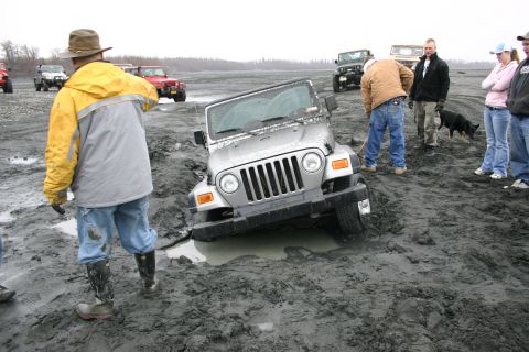 2003 Jeep TJ - A silver 2003 Jeep Wrangler is stuck in thick mud, with several people and other off-road vehicles gathered around.