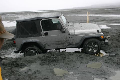 2003 Jeep TJ - A silver Jeep TJ is stuck in thick mud, with its front wheel submerged.