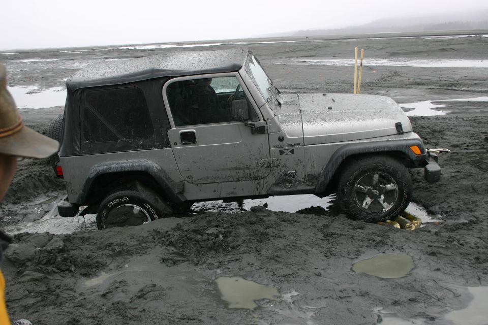 Silver Jeep TJ stuck in mud, front wheel deep, soft top on