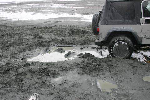 2003 Jeep TJ - A silver Jeep Wrangler is stuck in deep mud on a desolate, overcast day.