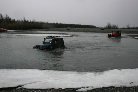2003 Jeep TJ - Jeep TJ navigates a water crossing, with another Jeep and a red vehicle in the distance.